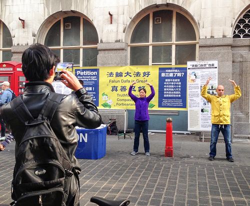 圖9：一位中國留學生模樣的年輕人經過法輪功學員的活動場地時停下腳步，認真攝下法輪功學員的煉功場面和真相橫幅。