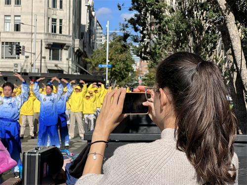 '圖4：法輪功學員集體煉功的場面祥和，吸引路人拿出手機拍照。'