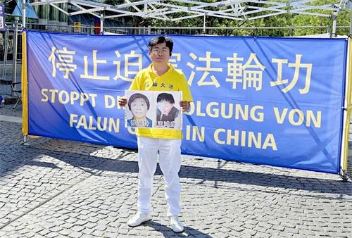'圖2：我在2025年7月19日德國法蘭克福的「7﹒20」紀念活動上舉著我熟悉的、2025年初相隔一個月去世的母女法輪功學員遺像，紀念那些在迫害中失去生命的法輪功學員。'